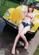 A woman in a bikini sitting on the hood of a yellow car.