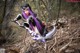 A woman with purple hair holding a sword in the woods.