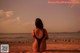 A woman in a black bathing suit sitting on a beach.